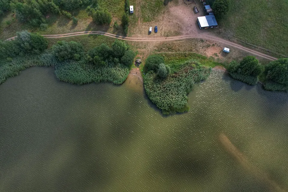 Drone capture of a serene rural campsite by the lakeshore with vehicles and tents.