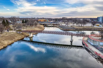 A tranquil view of a pedestrian bridge over a river reflecting the cloudy sky in Rochester, MN.